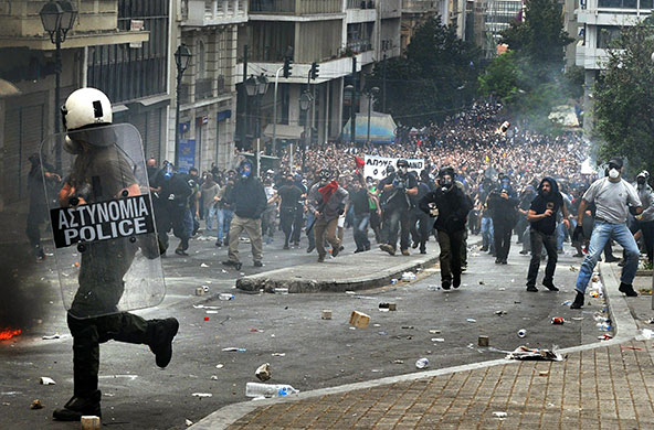 Greece Rioting: A Greek riot police officer runs to escape from protestors