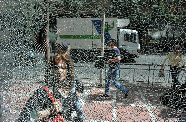 24 hours in pictures: Athens, Greece: A pedestrian looks at a broken shop window
