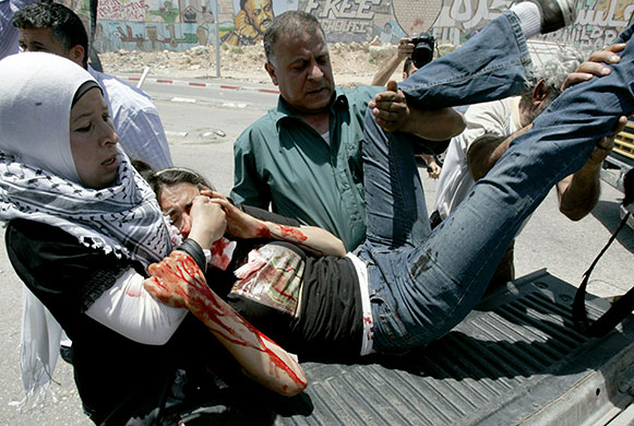 Israel protests: Palestinians carry a US peace acitivist, wounded by a tear gas grenade 