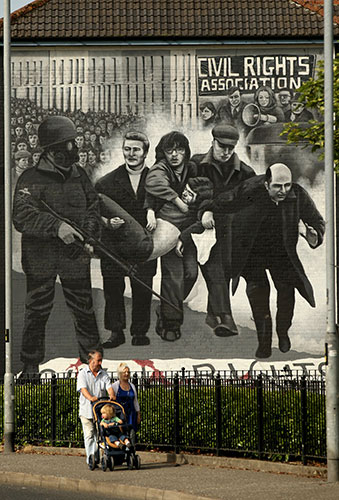 Bloody Sunday Inquiry: A family walk past a mural in the Bogside area of Londonderry