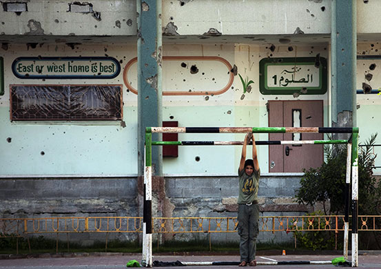 Summer Camp: Backdropped by a bullet-ridden wall, a Palestinian boy hangs on a goalpost