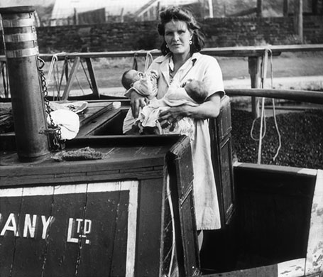 Longden's Canals: A woman stands on a canal boat holding two babies