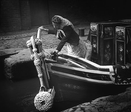 Longden's Canals: A woman with a headscarf steers the rudder of her boat