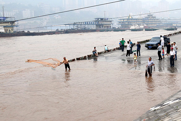 China flooding 2: A man on a submerged road throws a net to fish in the Yangtze River