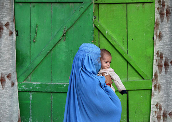 24 hours in pictures: A woman wearing burqa carries a child in Kabul