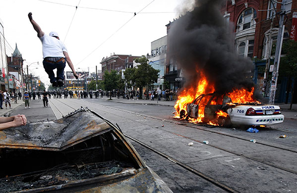24 hours in pictures: Toronto, Canada: A protestor jumps on a burned out police car