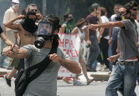 Greece protests: A demonstrator uses a slingshot during a clash with riot police