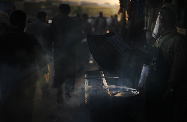 24 hours in pictures: Kabul, Afghanistan: A man fans coals as he barbecues meat at a market 