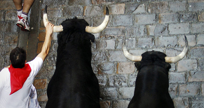 24 Hours: A runner holds on to the horn of a Dolores Aguirre bull in Pamplona
