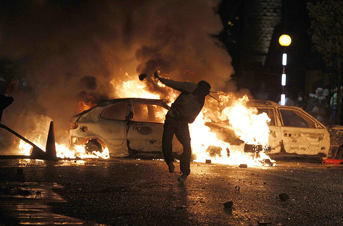 Belfast riots: A Nationalist youth standing near burning vehicles throws a missile