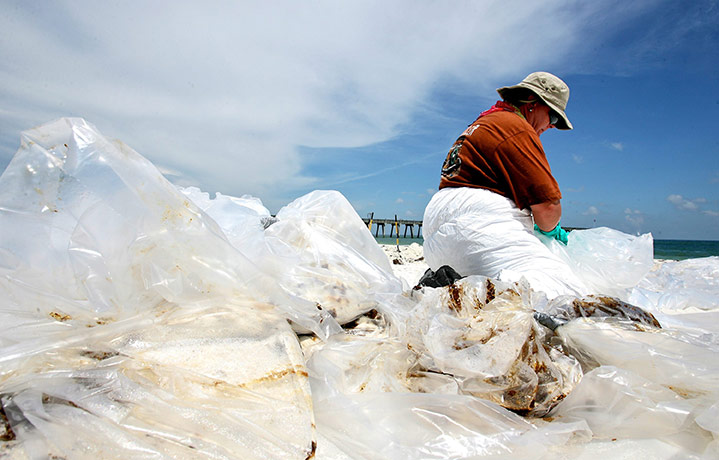 Deepwater Horizon: BP oil spill :  A clean up crew worker ties up bags full of oil and sand