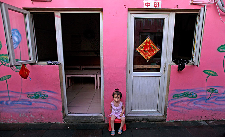 24 hours in pictures:  young Chinese girl looks on while sitting outside her kindergarten China