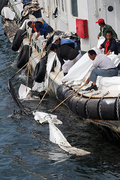 Dalian Oil Spill: Workers on a boat collect crude oil in the sea near Dalian
