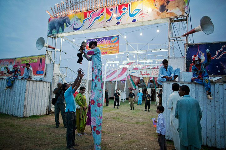 Jan Baz Circus: A stiltwalker holds a child aloft as members of his troupe lure customers in