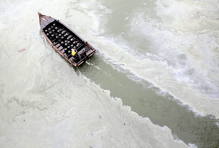 24 hours in pictures: Dalian, China: A boat travels through an oil spill site at a fishing port