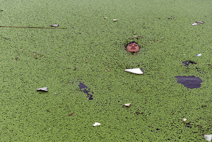 24 hours in pictures: Jiaxing, China: A boy floats on a river covered by duckweed