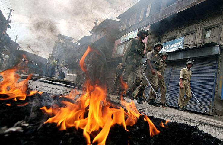 24 hours in pictures: Srinagar, India: Police walk past burning tyres