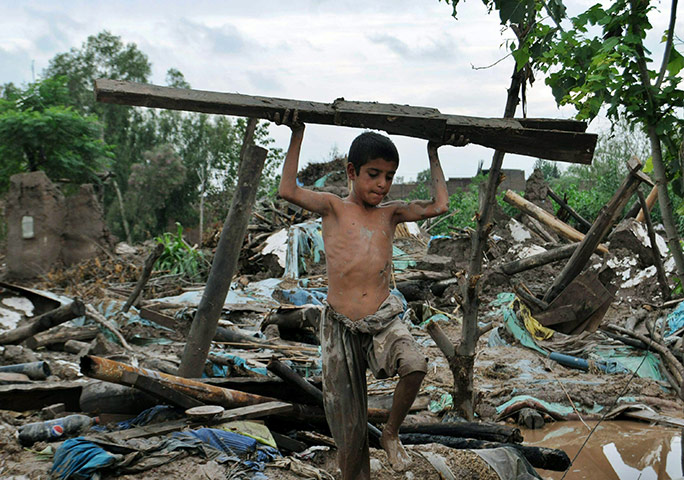 Pakistan floods: Boy removes wood from his collapsed house in the flood-hit area of Nowshera