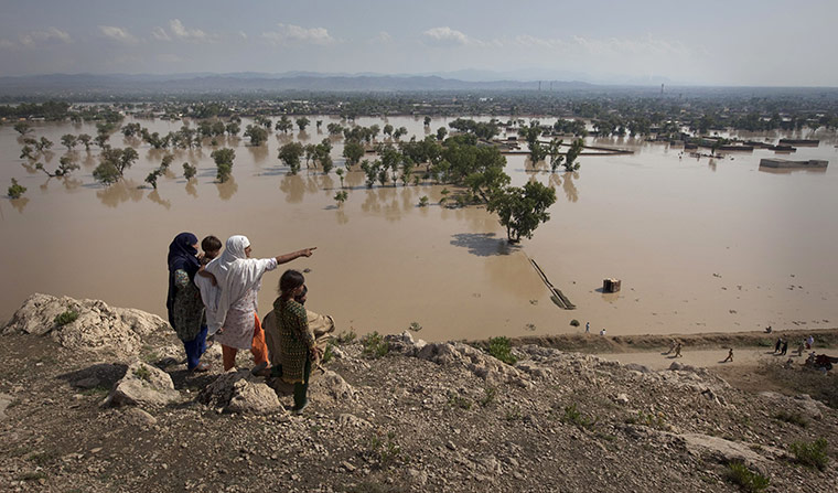 Pakistan floods: A person points towards their flooded home from a hilltop at Nowshera