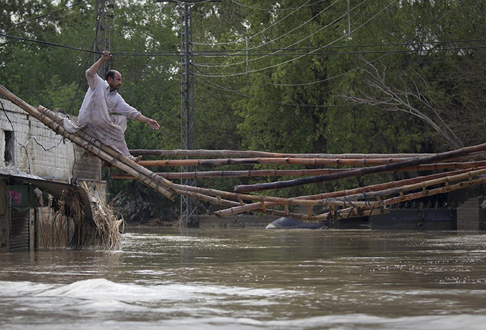Pakistan floods: A man crosses a makeshift bridge to escape his flooded home in Nowshera