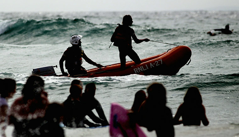 24 hours: Padstow, England:  RNLI lifeguards in a inflatable boat patrol the surf 