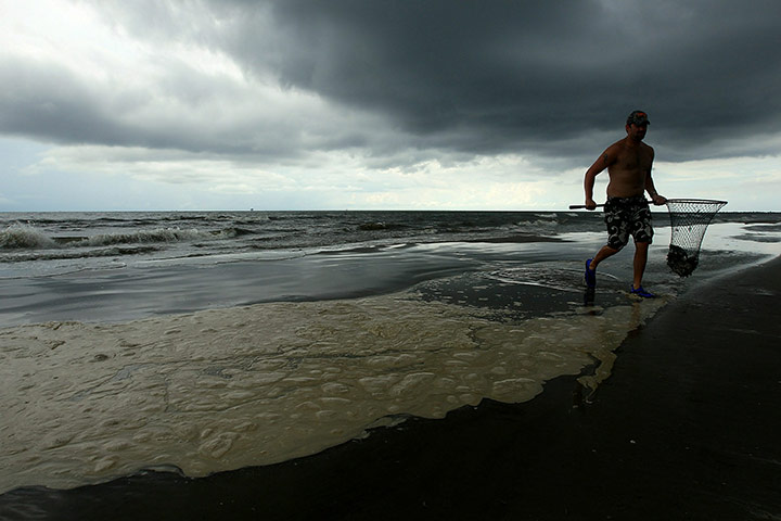 Week in Business: A man wades in from the ocean near a pool of dispersed oil