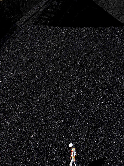 24 Hours in Pictures: A worker walks in front of a coal pile at a mining site in Indonesia