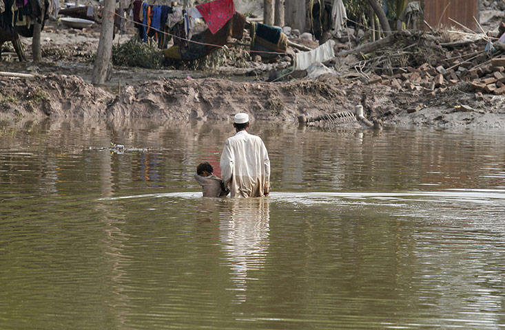 pakistan flooding: A Pakistani man holds on to his son as he wades through floodwaters