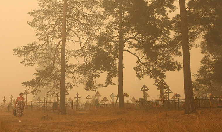 Forest fires in Russia: A woman walks in dense smoke near a cemetery in the village of Beloomut