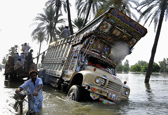 24 Hours in Pictures: A man passes a truck that slipped off a flooded road in Pakistan