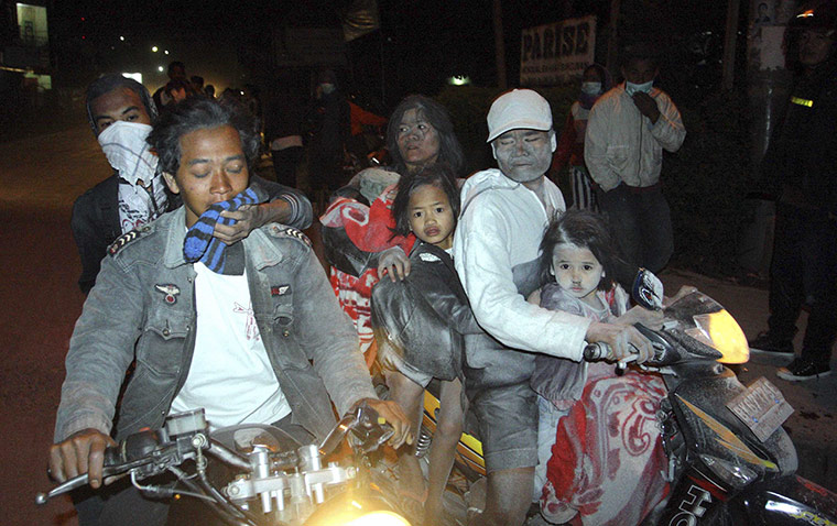 Sinabung volcano: Villagers covered in ash leave their village on motorcycles