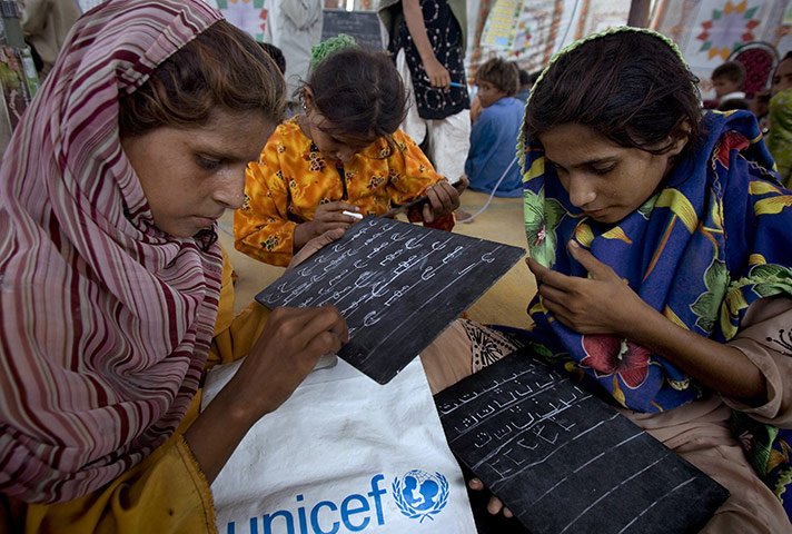 Pakistan Floods: Girls write over a small blackboard in a makeshift school in Pakistan