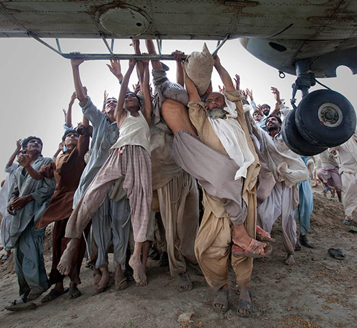 24 hours in pics: Pakistan flood victims grab the side bars of a hovering Army helicopter