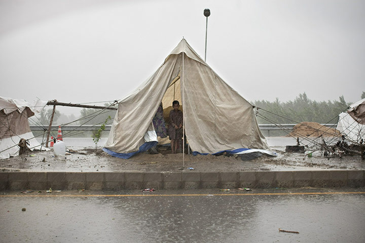 Pakistan update: A Pakistani boy shelters from heavy rain inside a tent erected on motorway