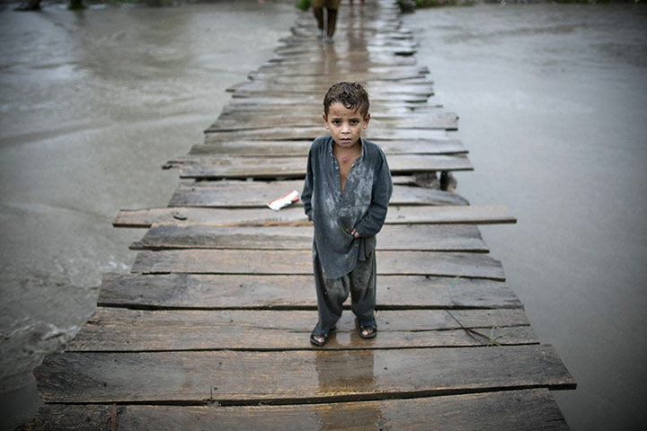 Pakistan update: Pakistani child walks on a wooden bridge towards the village of Shah Alam