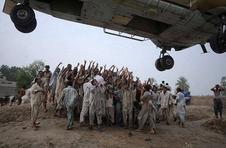 Pakistan update: Pakistani villagers raise hands to get food dropped from an army helicopter