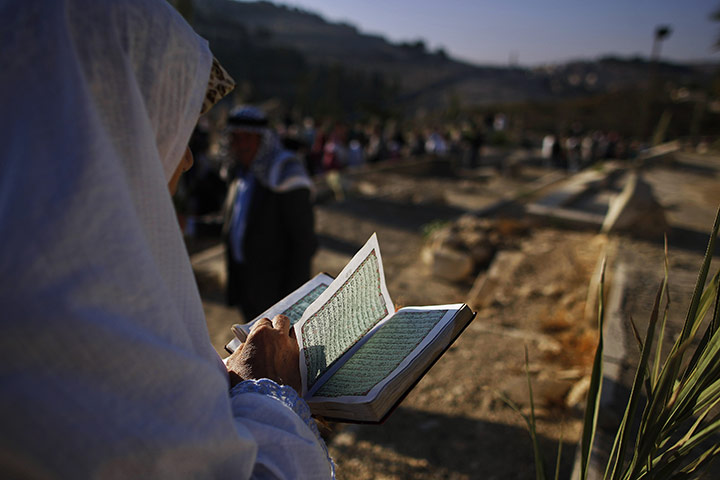 Eid begins: A Palestinian Muslim woman reads verses of the Qur'an over the grave