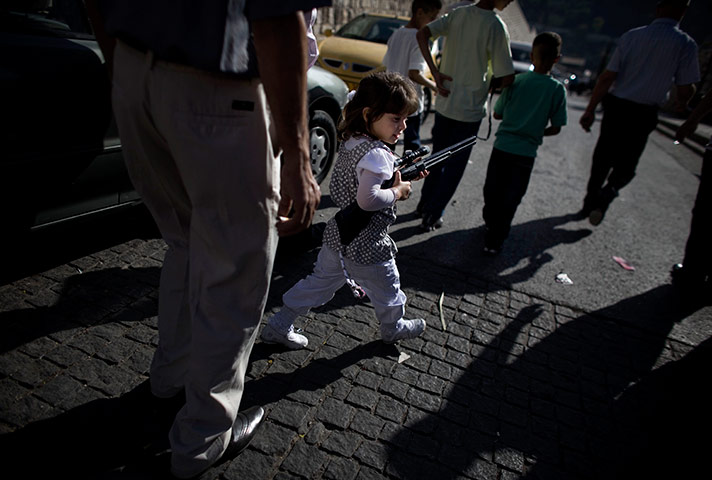 24 hours in pictures: A Palestinian girl plays with a toy gun as she walks during Eid al-Fitr 