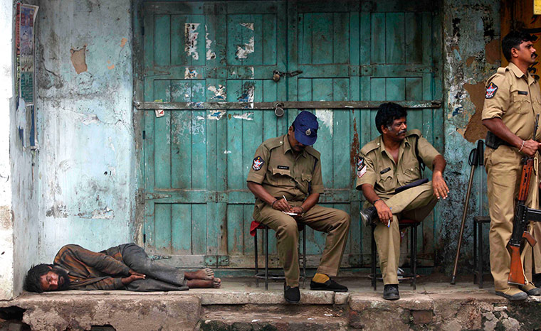 24 hours in pictures: A homeless man sleeps as Indian policemen sit outside a closed shop 