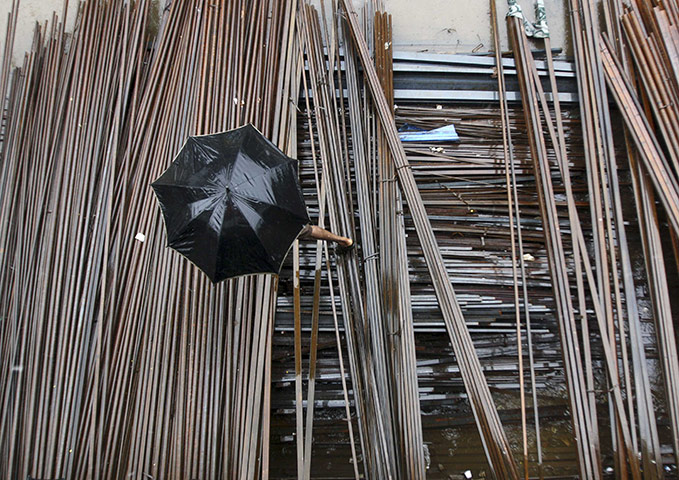 24 hours in pictures: A man carrying an umbrella walks on iron rods as it rains in Noida