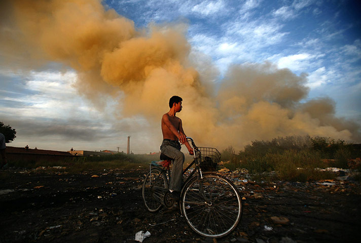 24 hours: Changchun, China: A boy on a bike stops by smoke from a waste foam fire 