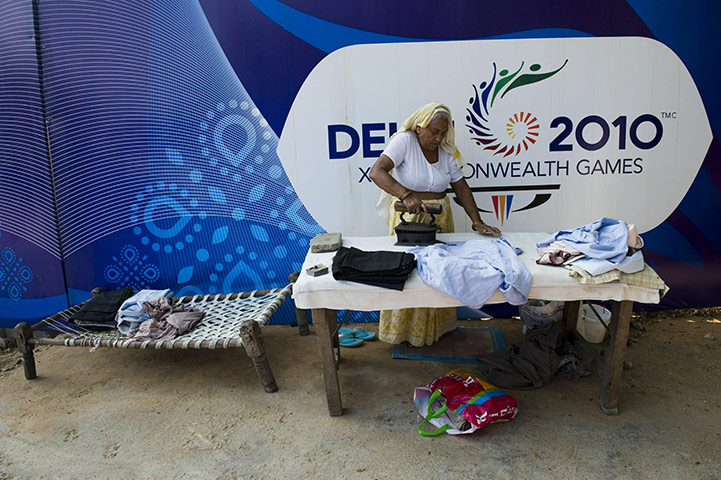 Commonwealth games: A woman irons clothes in front of a Commonwealth Games hoarding 