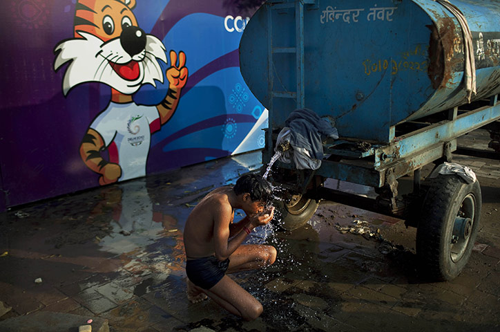 Commonwealth games: An Indian labourer washes in the street next to a camp for migrant workers 