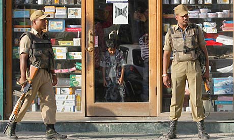 Indian policemen stand guard as Kashmiri people shop during a relaxation of curfew in Srinagar