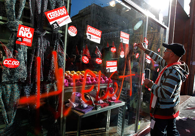 European strikes: A picketer places stickers for the strike on the window of a shop, Spain