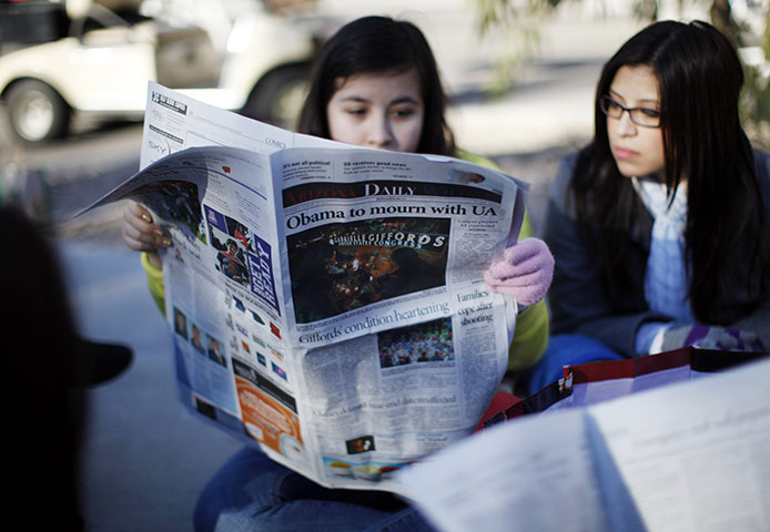 Tuscon shooting: Women waiting in line for a memorial service for victims look at the paper