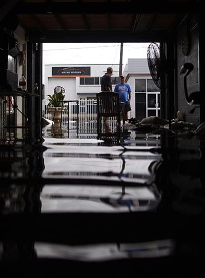 Aerials Brisbane floods: Two men stand in the entrance of a flooded car repair workshop in Brisbane