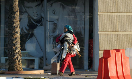 A Tunisian woman carrying clothes walks past a looted supermarket