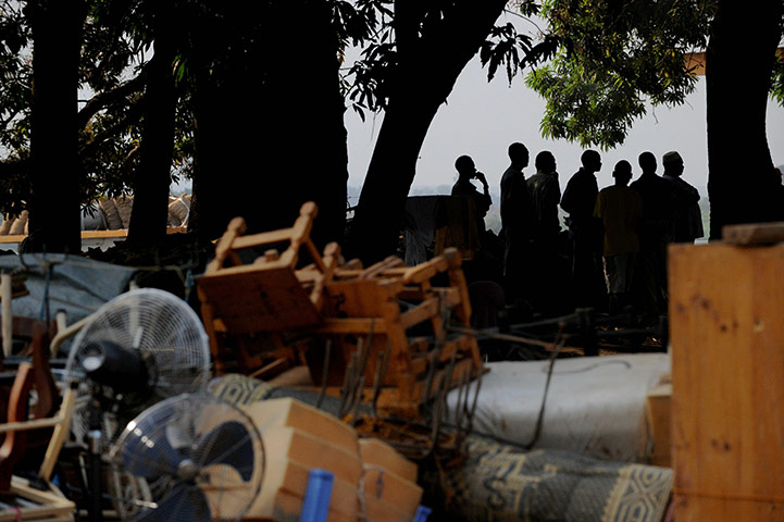 Sudan election: Men stand in the shade of trees near a pile of belongings at a camp