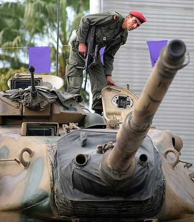 Tunisia uprising: A Tunisian soldier stands guard on a tank facing demonstrators